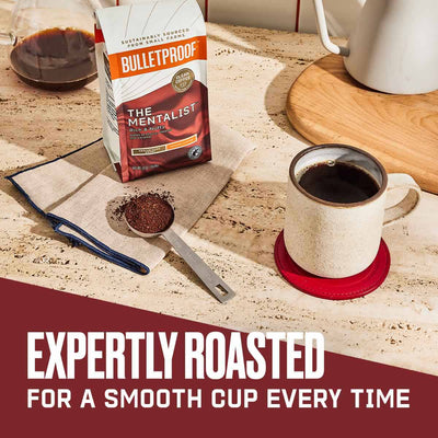 Expertly Roasted for a smooth cup every time. A bag of Bulletproof Mentalist Ground Coffee with a cup of coffee next to it and a scoop of ground coffee. 