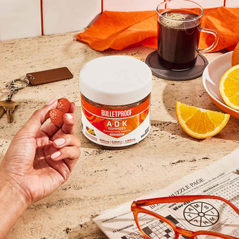 Hand holding  A+D+K Gummies on kitchen counter top with coffee