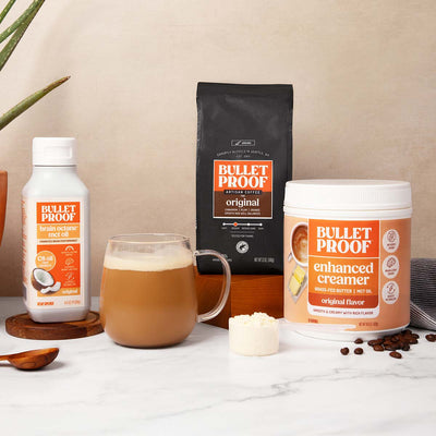 Bulletproof coffee setup with coffee, creamer, and oil on a white surface.