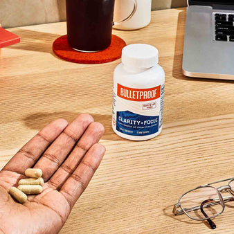 hand holding 4 capsules of clartiy+focus next to a bottle of Bulletproof Clarity + Focus.