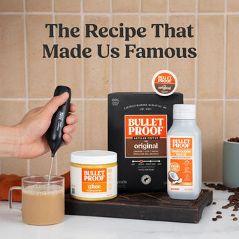 Bulletproof coffee setup with coffee pods, ghee, and mct oil on a tiled wall background with hand frothing a mug of coffee
