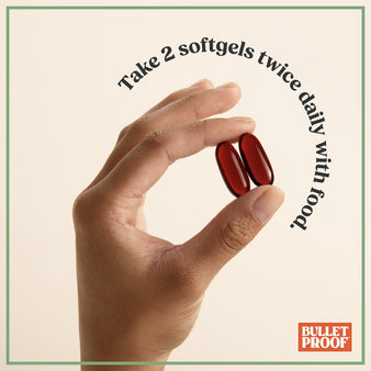 Hand holding two red softgels with text on a beige background, featuring the Bulletproof logo.
