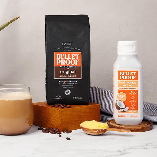 Bulletproof coffee setup with coffee beans, coffee bag, and oil bottle on a wooden coaster.