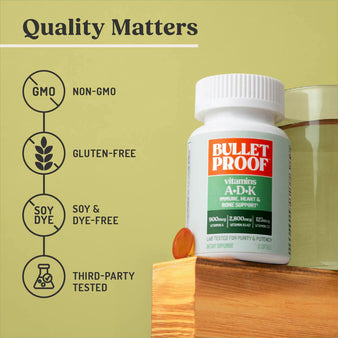 Bulletproof vitamins a-d-k bottle on wooden pedestal next to water glass and softgel, non-gmo, gluten-free, soy and dye-free, third-party tested