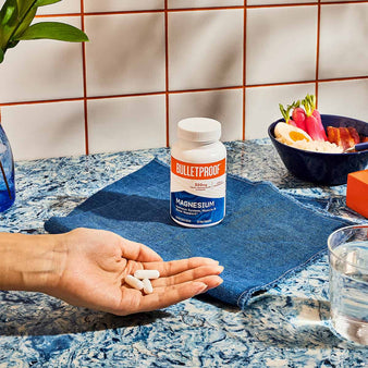 3 capsules of Bulletproof Magnesium resting on palm of hands next to a bottle of Magesium.