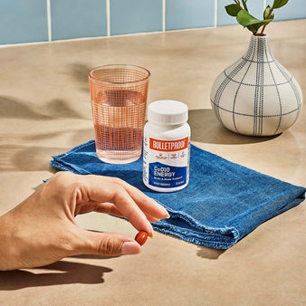 Bulletproof CoQ10 Energy pinched between fingers next to a bottle of CoQ10 Energy.