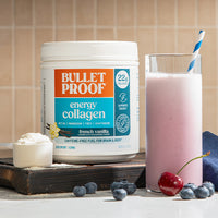 Bulletproof energy collagen container with a glass of pink smoothie and berries on a wooden surface.