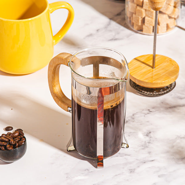 French press with coffee on a marble surface next to a yellow mug and coffee beans.