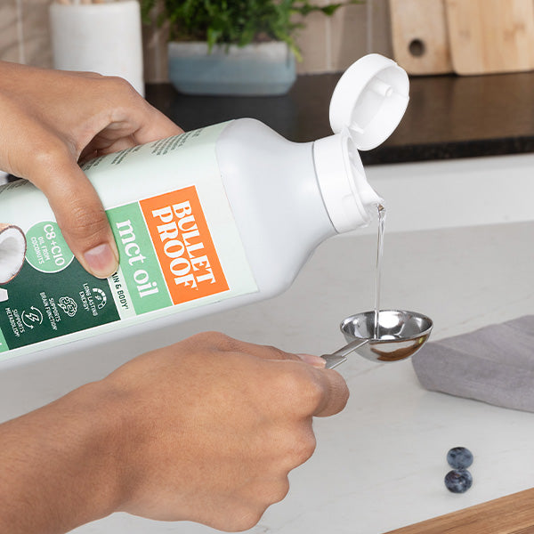 Person pouring Bulletproof MCT oil from a bottle into a spoon on a kitchen counter.