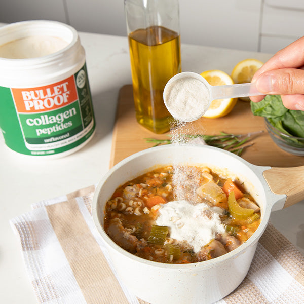 Person adding Bulletproof collagen peptides to a bowl of soup on a kitchen counter.