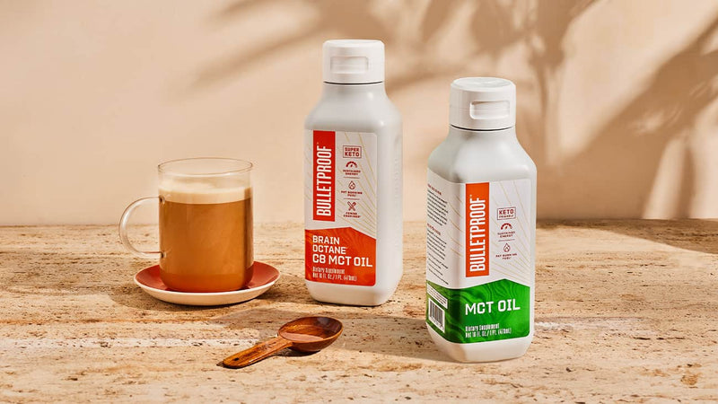 A cup of Bulletproof coffee next to a bottle of MCT Oil and a bottle of Brain Octane Oil