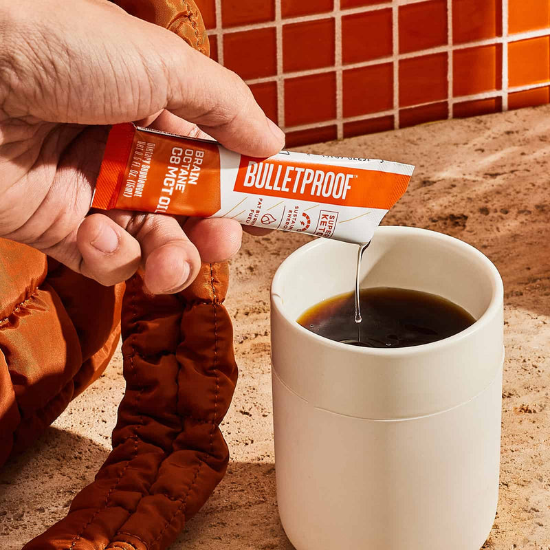 Hand pouring on-the-go packet of Bulletproof Brain Octane C8 MCT Oil into a cup of black coffee