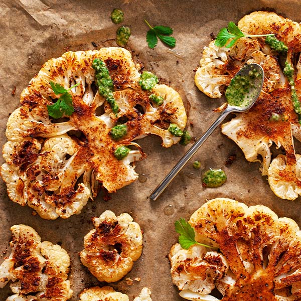 Roasted cauliflower with green sauce on a brown surface