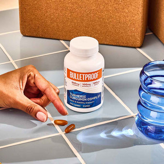 Hand reaching for Bulletproof Turmeric Curcumin capsules next to a bottle of Bulletproof turmeric curcumin complex