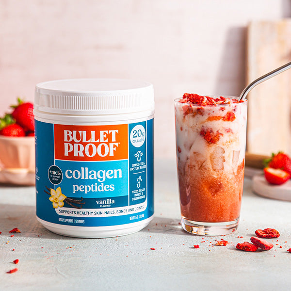 Bulletproof vanilla collagen peptides container next to a strawberry smoothie