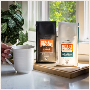 Two bags of Bulletproof coffee on windowsill next to mug of coffee