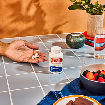 Hand holding 3 capsules of Bulletproof Zen Mode with Zen mode and a cup of water.